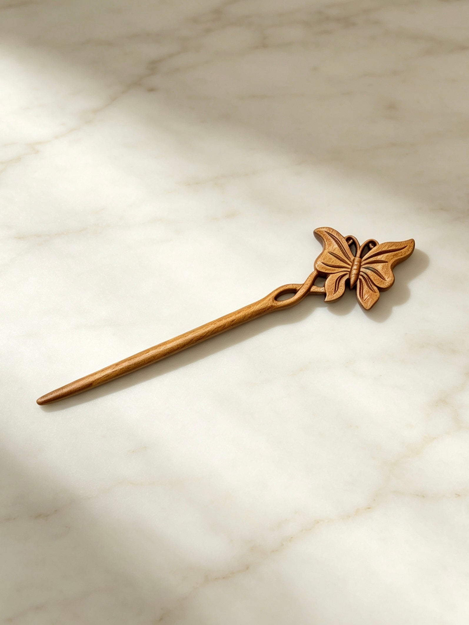 Butterfly carved hair stick displayed on a marble surface
