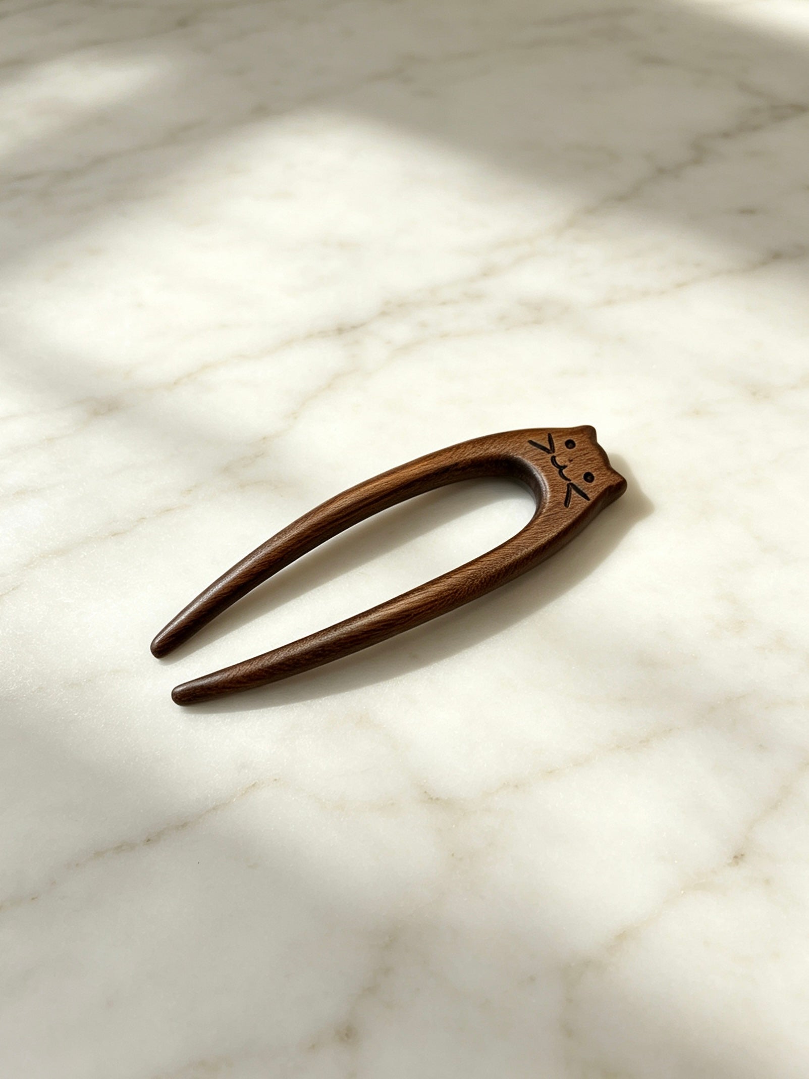 Cat double-prong sandalwood hair fork displayed on a marble surface