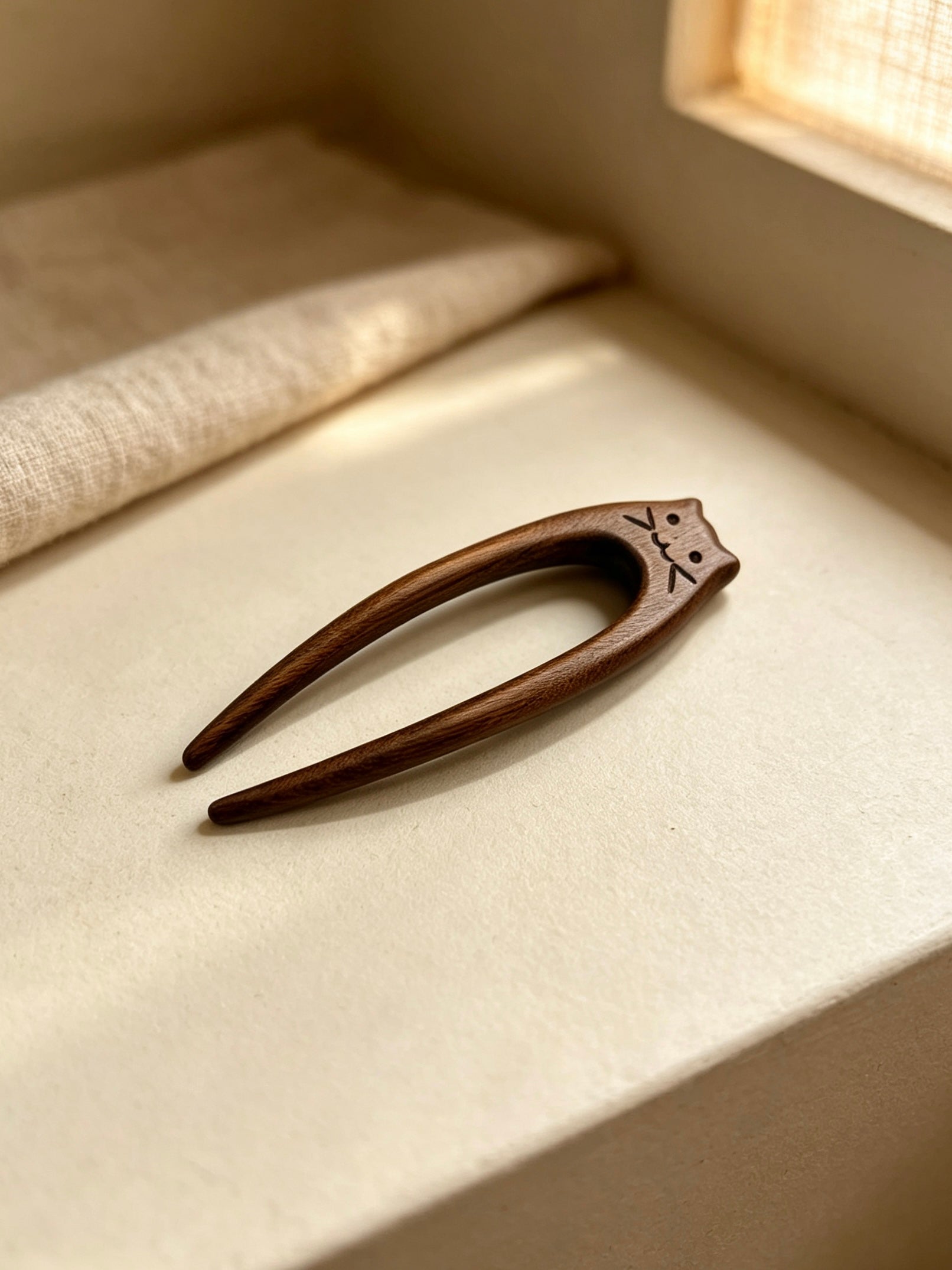 Cat double-prong sandalwood hair fork displayed on a light fabric surface