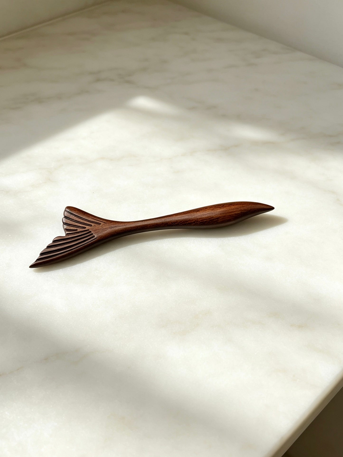 Fish tail sandalwood hair stick displayed on a marble surface