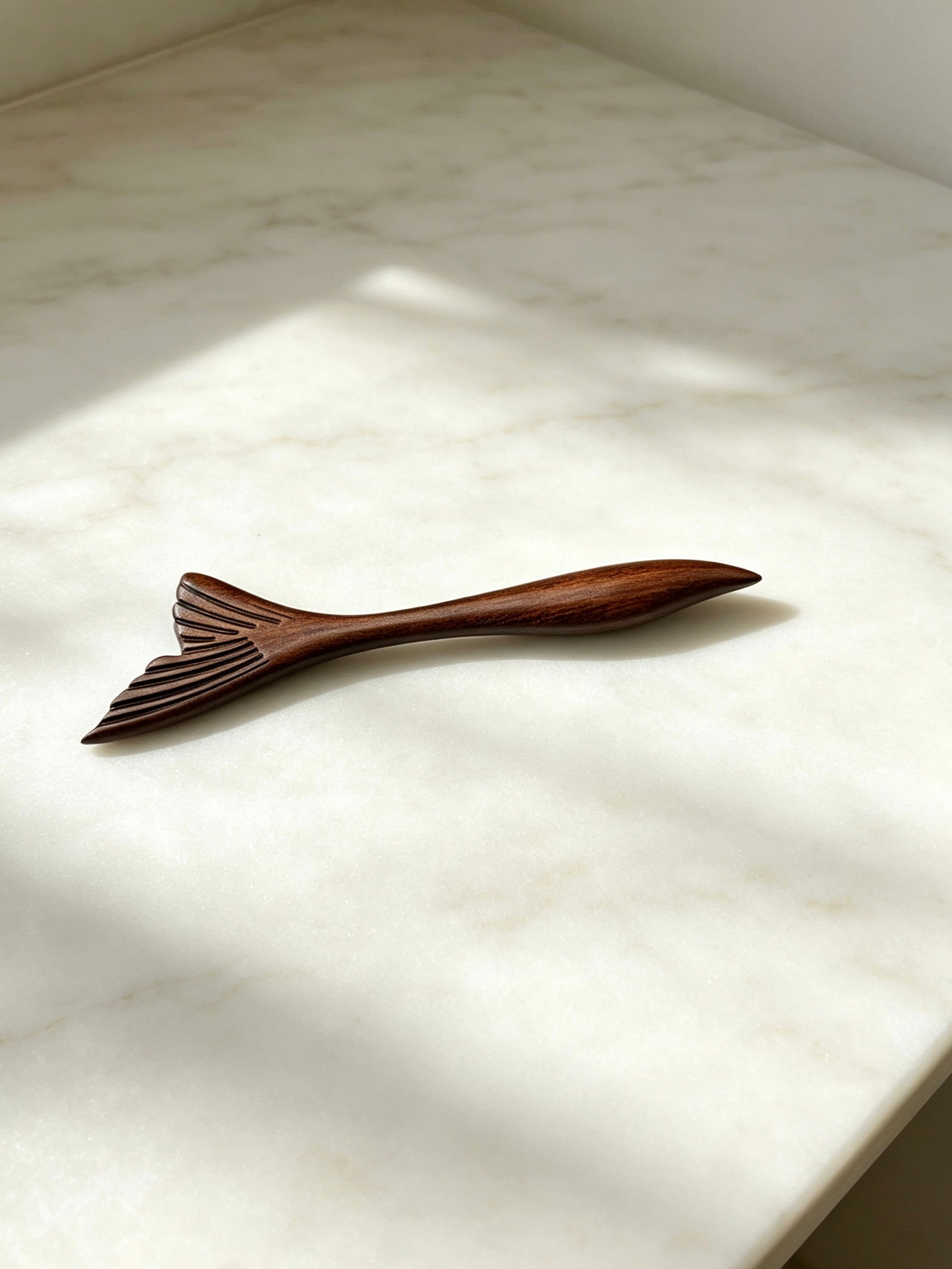Fish tail sandalwood hair stick displayed on a marble surface